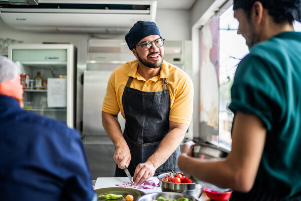 Colleagues during cooking class or working in a restaurant chef slicing and chatting