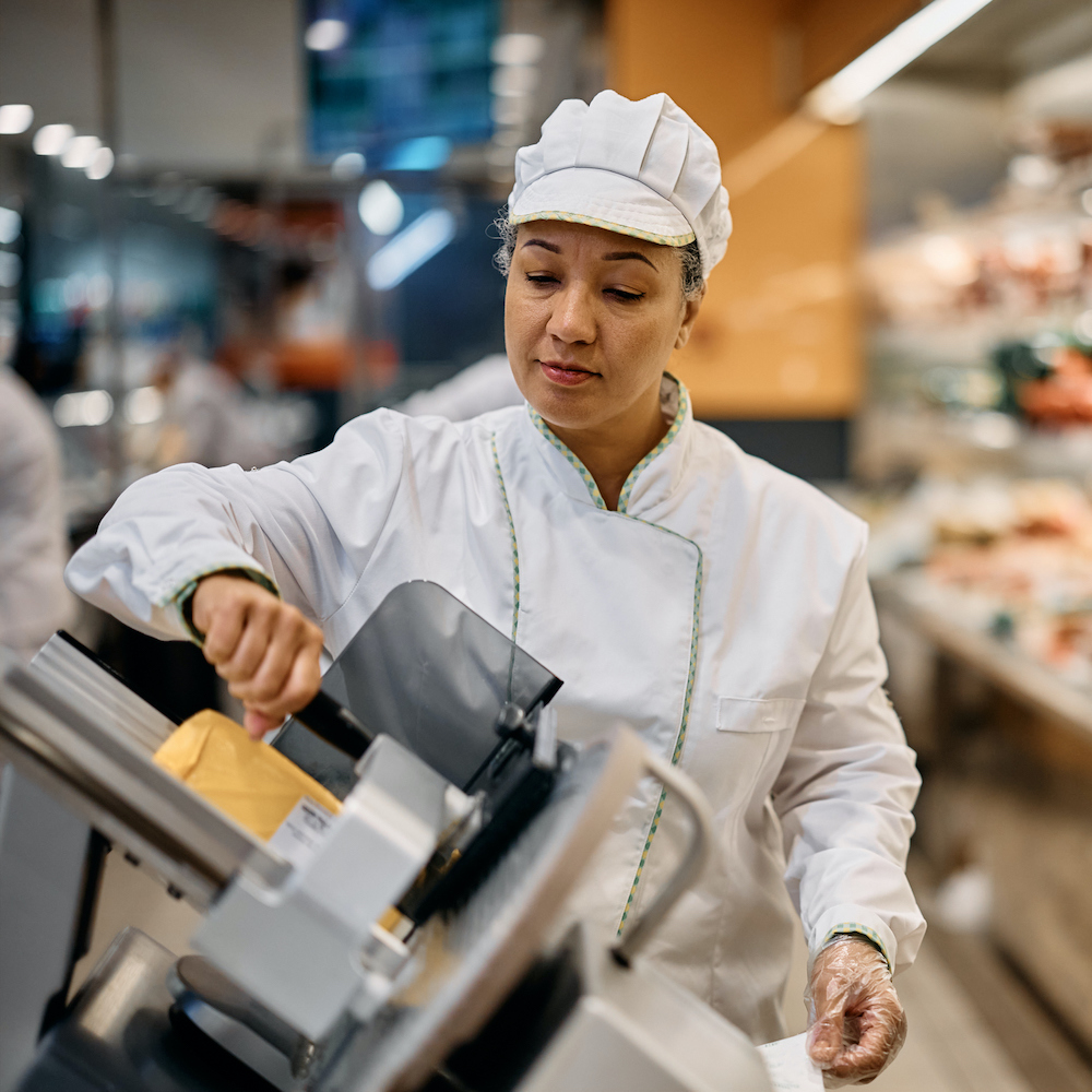 woman in white uniform slicing meat in deli