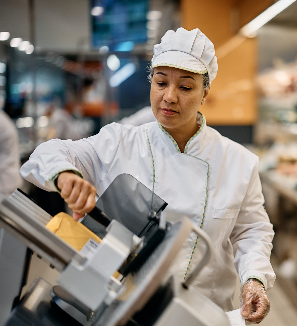 Supermarket worker using a slicer at delicatessen section.