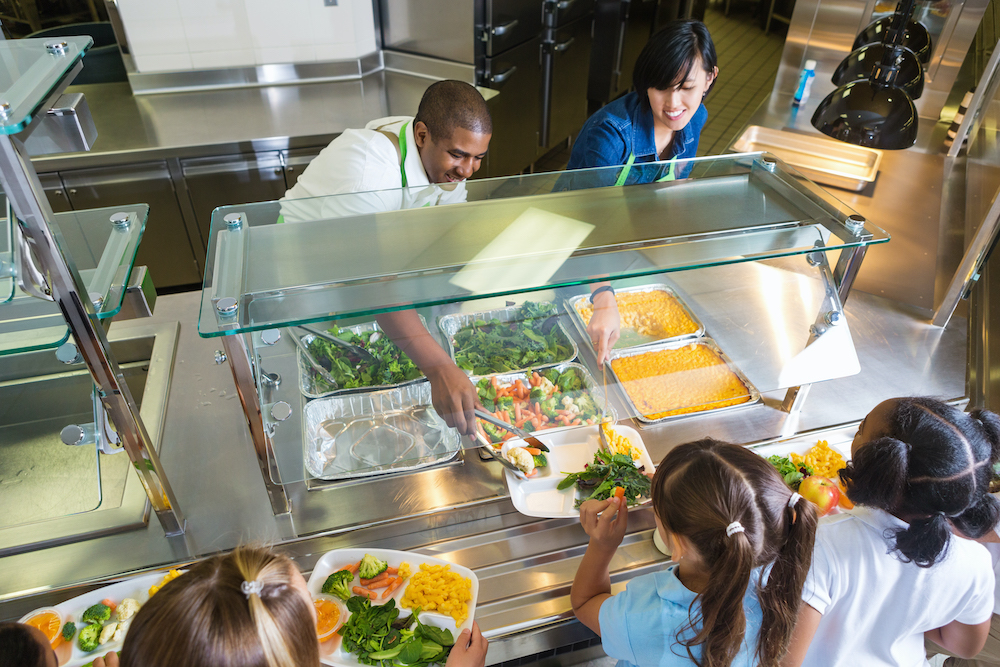 Cafeteria worker serving trays of healthy food to children